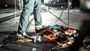 Guitarist in brown shoes stands beside a pedalboard onstage