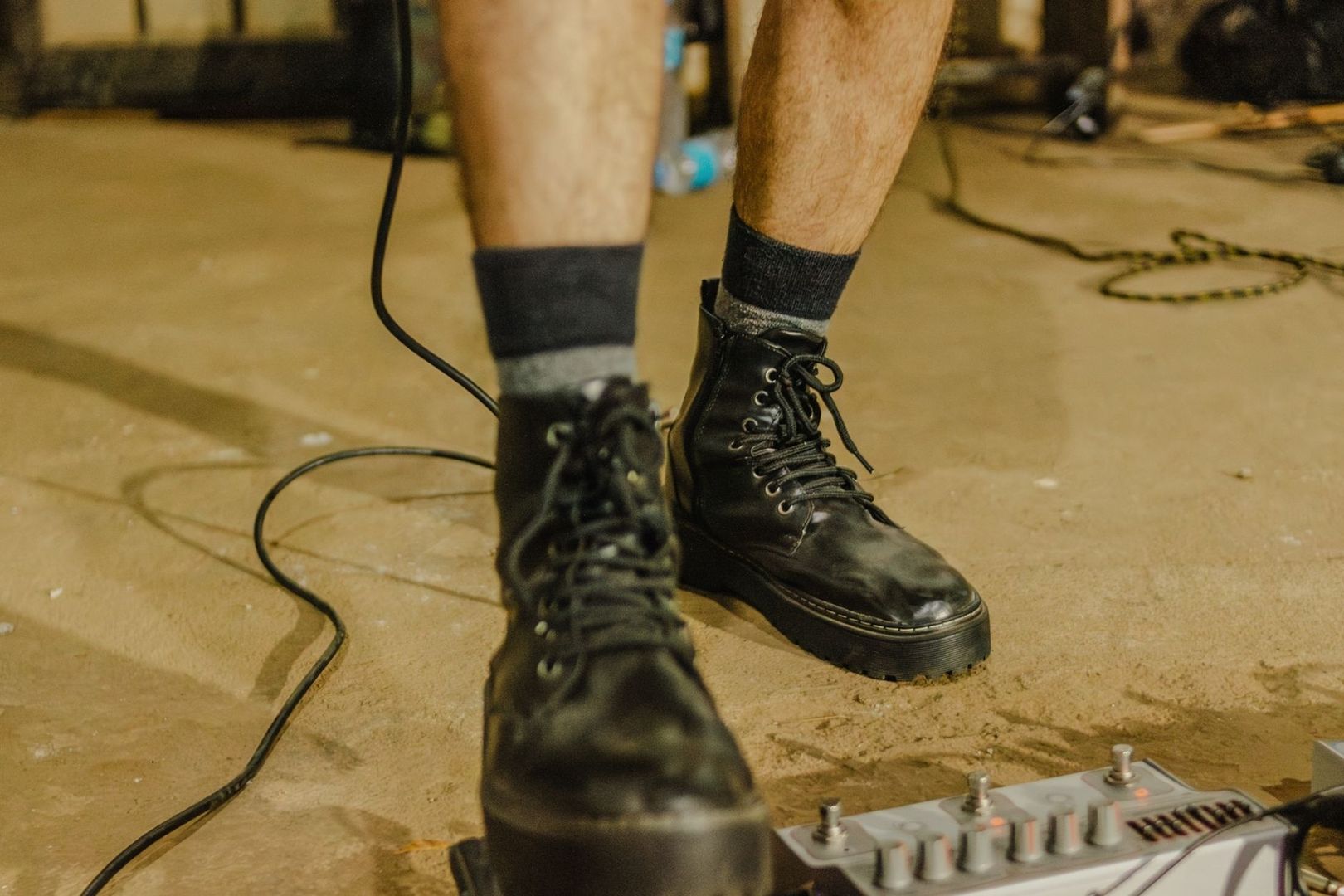 Black leather boots beside a guitar pedalboard on a stage floor